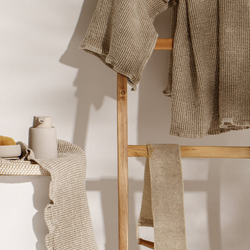 Soft linen and cotton bath towels and bathrobes beautifully displayed in a serene, natural bathroom setting.