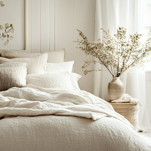 Natural linen and cotton bedding and throws styled in an airy, serene bedroom designed for restful, elegant comfort