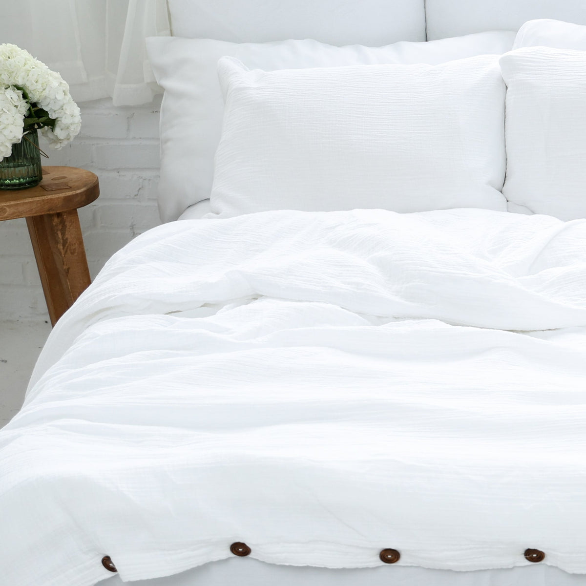 White organic pillow cases and duvet cover on a bed with a wooden side table and decorative elements.