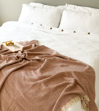 Cinnamon blanket draped over a bed with white bedding and pillows.