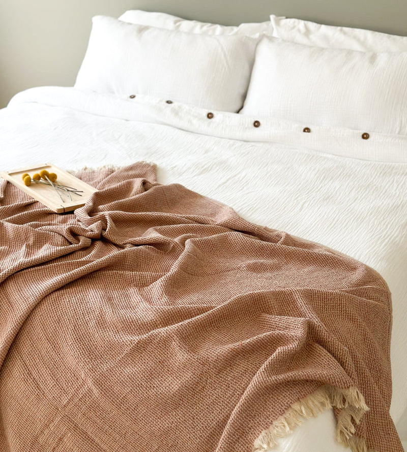 Cinnamon blanket draped over a bed with white bedding and pillows.
