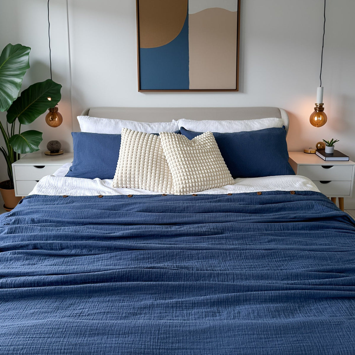 Bedroom with a bed featuring blue and white bedding, organic duvet cover, decorative pillows, and a painting on the wall.