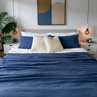 Bedroom with a bed featuring blue and white bedding, organic duvet cover, decorative pillows, and a painting on the wall.