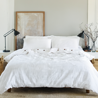White bedroom with a neatly made bed with white organic duvet cover, lamps, and baskets.